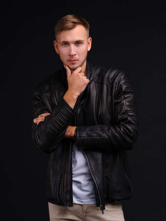 A guy posing on a black background holding his hand to his chin.の写真素材