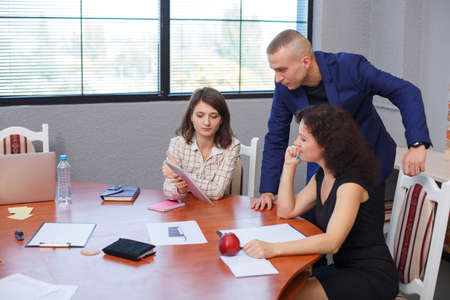 In the office. The girl shows something on the tablet to other office workers.の写真素材