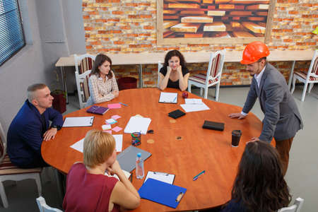 Meeting at the office. At the round table the team sits, and next to it there is a chief in a...