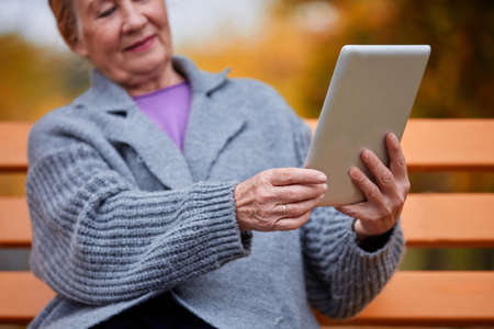 Grandmother with a tablet on a bench in the parkの写真素材