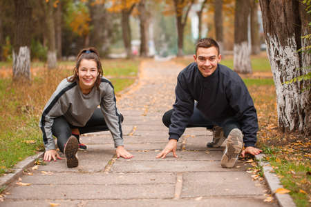 A couple stretches their leg muscles in a park in the fall.