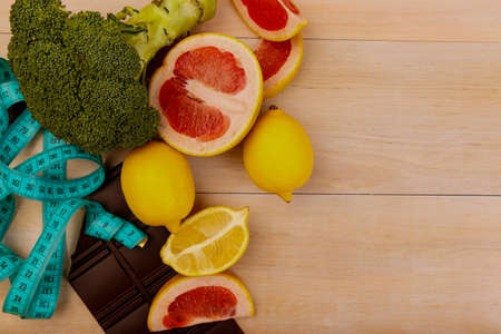 Fruits such as lemon, grapefruit sliced and vegetables pepper, hot pepper, broccoli and chocolate bar with tape for measuring for a healthy diet on a beige table. View from aboveの写真素材