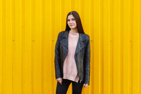 White girl in a black jacket posing outdoor near with yellow wallの写真素材