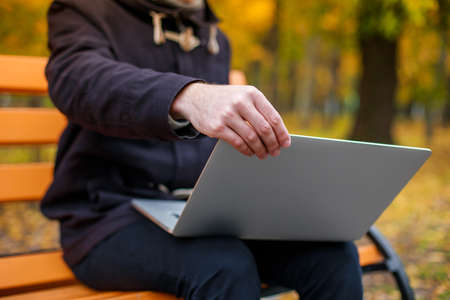 Hands of a guy holding a laptop in the park on a benchの写真素材