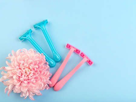 Set for hair removal. Blue and pink womans razor on the blue background. Beautiful roses and pionies lying near the razors. Close-up of objects.の写真素材