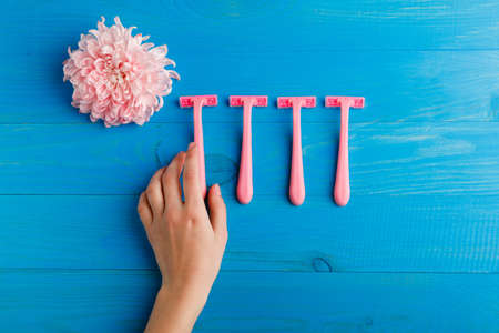 Set for hair removal. Blue and pink womans razor on the blue background. Beautiful roses and pionies lying near the razors. Close-up of objects.の写真素材