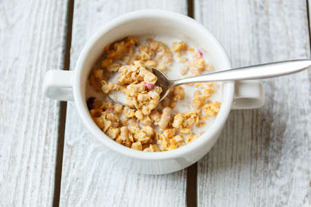 Oatmeal porridge with milk, walnuts, blueberries in a white bowl on the light wooden background....