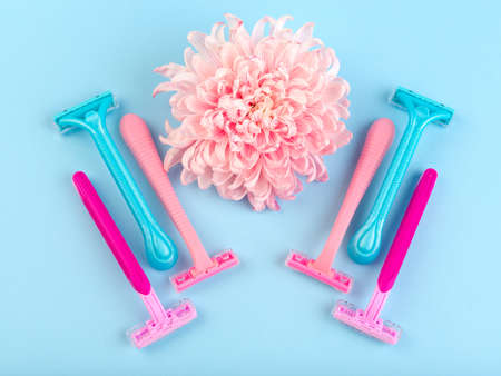 Set for hair removal. Blue and pink womans razor on the blue background. Beautiful roses and pionies lying near the razors. Close-up of objects.の写真素材