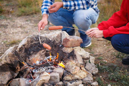 Young people fry appetizing sausages on a flaming fire. Outdoors.の写真素材