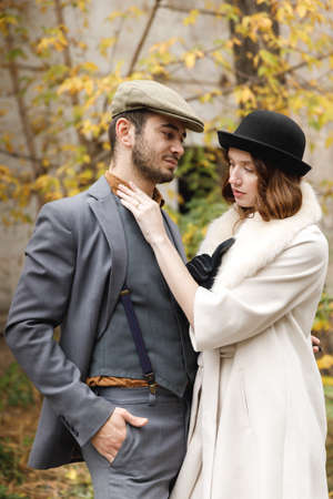 A loving retro gangsters couple are standing outside and hugging. The girl is straightening the guys collar. Outdoors.の写真素材