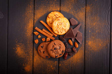 Oat and chocolate biscuits, black chocolate, nuts, raisins and a few cinnamon sticks of a wooden table. Around the grated cinnamon. Inside. View from above.の写真素材