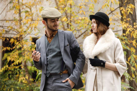 A retro gangster couple are walking around holding hands and looking at each other. The guy is smoking a cigar. Outdoorsの写真素材