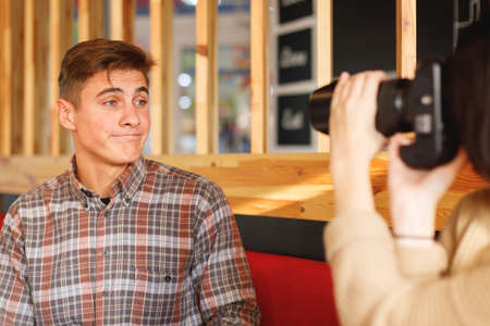 A couple is sitting in a cafe. The girl takes pictures of a guy who grimaces a camera. Inside.の写真素材