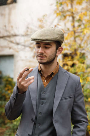 A man with a stubble, in a suit and hat, stands outside and smokes a cigar . Retro. Outdoors.の写真素材