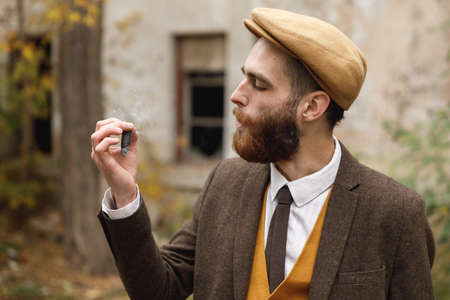 Gangster with a beard looks at the almost smoked cigar. Retro. Outdoors.の写真素材