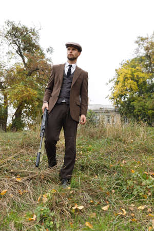 A dangerous gangster goes to somewhere with a gun in hands and looks out for someone. Retro. Outdoors.の写真素材