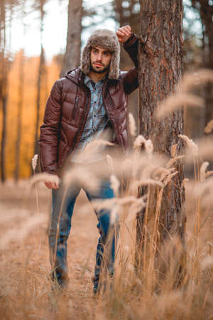 Caucasian guy rested his elbow on a tree in the autumn forest