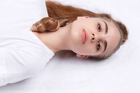 A white girl lies, and a snail crawls along her neck in a white backgroundの写真素材