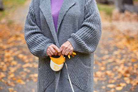Close-up of grandma's hand with orange leash and yellow leaves in hands in gray coatの写真素材