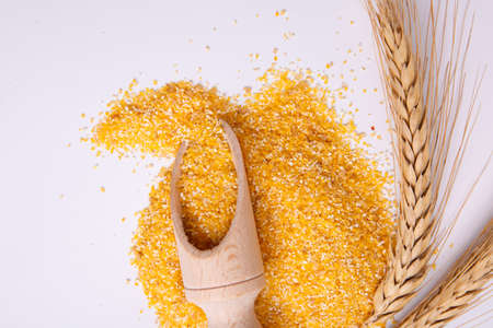Corn, appetizing, yellow groats isolated on white background with a branch of wheat and a wooden scoop. Top view, close-up.の写真素材