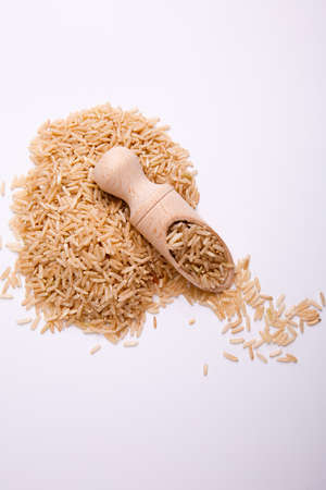 Untreated long rice in a wooden scoop on a white background, on white background, top view.の写真素材