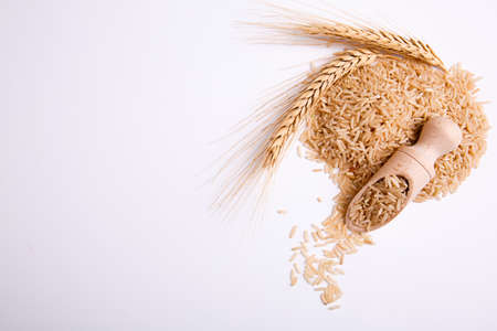 Brown brown rice on a white background with a wooden scoop filled with rice, close up is a sprig of wheat on white background. View from above. Free space for textの写真素材
