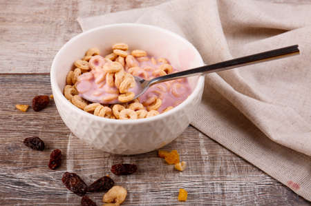 Breakfast, in a corrugated plate corn rings with yogurt, a spoon with rings over a plate, scattered raisins on a wooden background.の写真素材