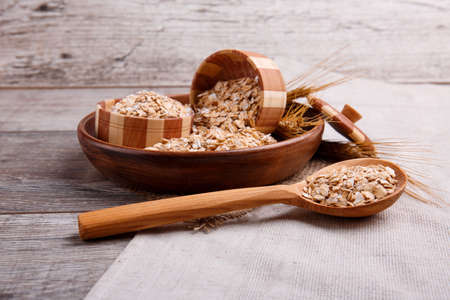 A composition with raw oat flakes in a bowl with a wooden spoon in which the oatmeal is on a...