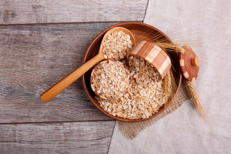 A composition with raw oat flakes in a bowl with a wooden spoon in which the oatmeal is on a...