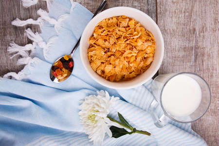 In a bowl of cornflakes, a spoon lies next to it and there is a glass of milk, on a wooden...