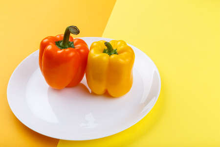 Bulgarian pepper on a plate on a yellow and orange background. Top view from an angle close-upの写真素材