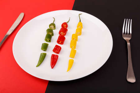 Hot pepper sliced on a plate on a red black background at an angleの写真素材