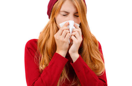 Redhead girl in red sneezes and wipes her nose on a white isolated backgroundの写真素材