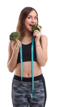 Fitness girl holds pepper at her mouth and in another broccoli on white isolated backgroundの写真素材
