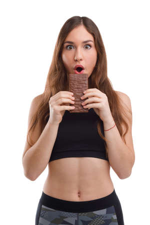 Fitness girl with surprise wants to bite a chocolate bar on a white isolated backgroundの写真素材