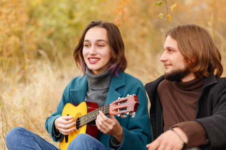 The guy looks like a girl playing on a ukulele in the autumn forest close-upの写真素材