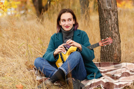 A girl with a ukulele sitting on a blanket in an autumn forestの写真素材