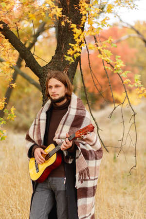 Young guy playing guitar on autumn backgroundの写真素材