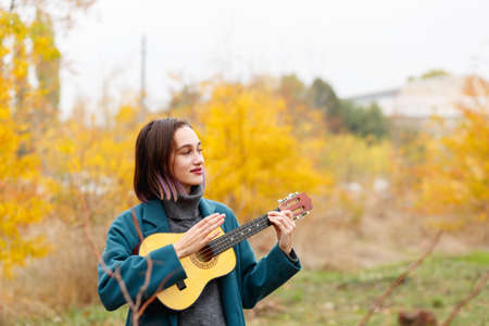 A brunette girl playing on a ukulele on an autumnal forest backgroundの写真素材