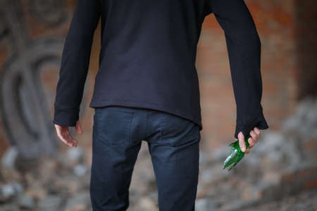 A broken beer bottle in the mans hand, against a brick wall used as a weaponの写真素材