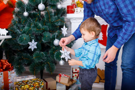 A happy father and his young son decorate the Christmas tree with white snowflakes.の写真素材