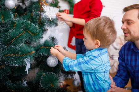 A happy father and his sons decorate the Christmas tree at home.の写真素材