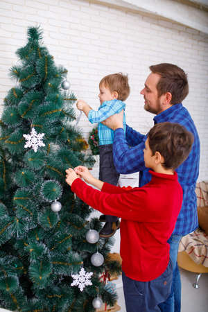 A happy father and his sons decorate the Christmas tree at home, a happy childhood.の写真素材