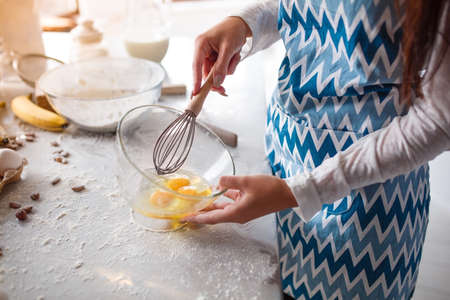 Close-up photo of a girl's hand with a broom. Woman in the kitchen in a blue apron is going to stir...