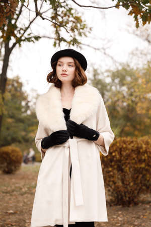Retro gangster girl in black hat and coat in autumn park looks asideの写真素材