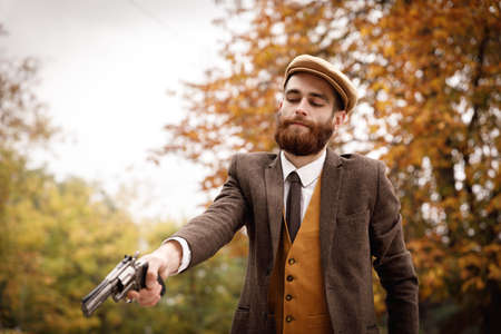 Retro gangster with a beard in an autumn park with a gun.の写真素材
