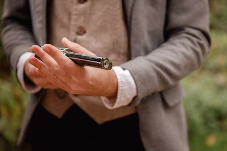 Close-up of a gangster hand with arms in the park. A man in a gray jacket holds a gun in his hands. Retro. On open air.の写真素材