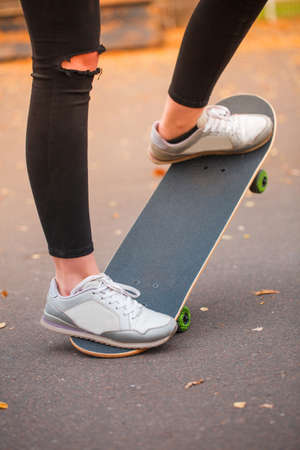 Close-up of a skateboarder's foot in black krosovkah on a skateboard, among the autumn leaves, a...