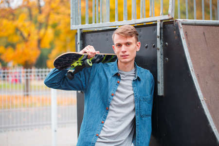Portrait of a handsome guy standing with a skateboard in his hands.