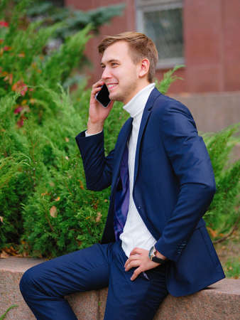 Young businessman in a suit outdoors with phone in hands.の写真素材